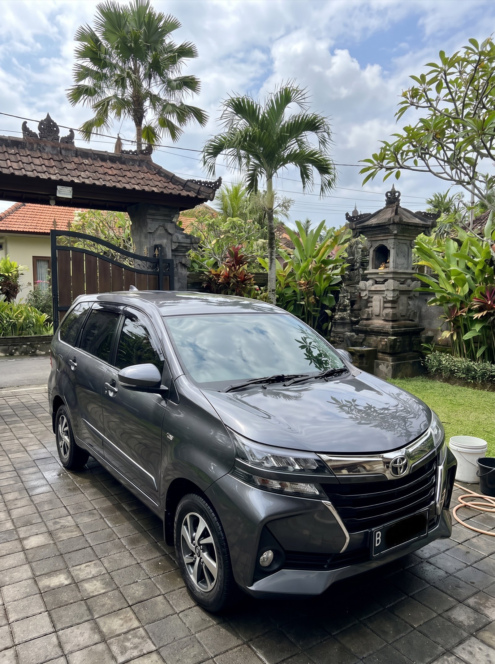 Freshly washed grey car in a Bali villa driveway, wash bucket and hose beside it